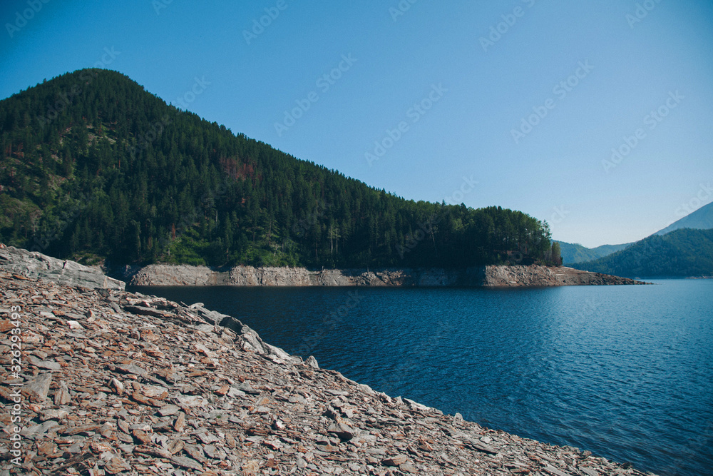 Wall mural the concept of boating, recreation, travel - splashes of blue water in the river, mountains, sky, stone shore. Copy space