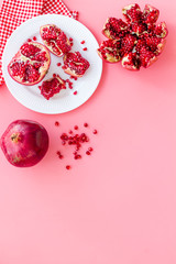 Juicy pomegranate with seeds on plate on pink table top-down copy space