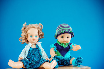 Old-Fashioned baby Doll dressed in knitted costume sits on shelf on blue background