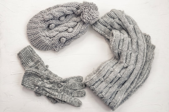 Warm female gray knitted gloves, scarf and hat on white textured  background. Flat lay, top view minimal fashion concept.