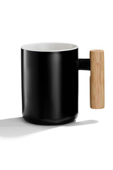 Subject shot of a black ceramic mug with a white inner surface and a wooden handle. The deep mug is isolated on the white background with shadows. 