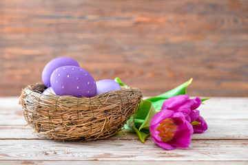 Nest with beautiful Easter eggs and flowers on table