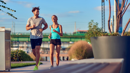 Modern woman and man jogging / exercising in urban surroundings near the river.