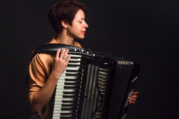 A brunette in a gold shirt, with short haircut, on a dark kground of the Studio. With accordion...