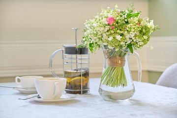 Table with white tablecloth tea in teapot, cups and bouquet of beautiful flowers
