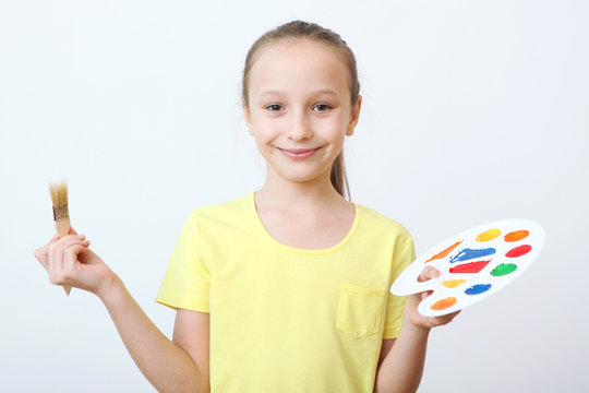 Cute happy girl with a palette for paints and a brush on a light background.