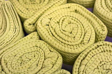 A pile of folded green bedspreads. Large rolls of rugs stand on their sides, texture effect.