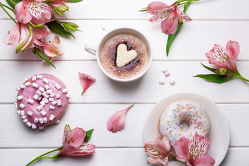 A cup of coffee with heart-shaped cookies and pink eustoma flowers on a white wooden background. View from above