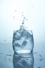 Ice falling glass of water, a splash of ice cube with splashes, pure drinking water in a transparent glass
