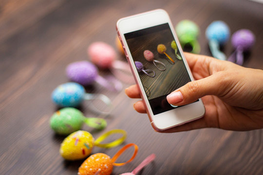 Woman makes a photograph of the colorful easter eggs with her cell phone. Mobile photo. Copyspace and place for text and wording. Easter concept.