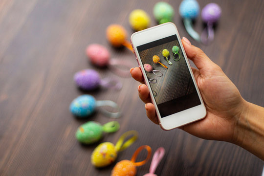 Woman makes a photograph of the colorful easter eggs with her cell phone. Mobile photo. Copyspace and place for text and wording. Easter concept.