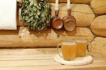 Two glass mugs of light beer in the interior of sauna among copper accessories. 
