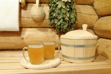 Two glass mugs of light beer among wooden accessories in the interior of sauna.
