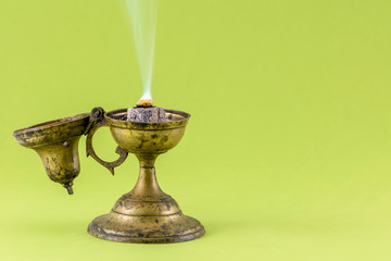 Old frankincense burner with burning frankincense on hot coal. Isolated on color background, copy space for text. Traditional method for incense burning.