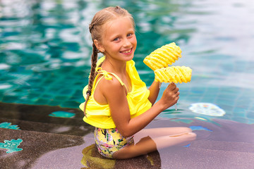 Cute baby girl in the pool. Little girl with pineapple in a tropical resort swimming pool.