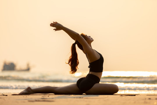 Happy Asian woman wearing black sport wear practice yoga Pigeon pose on the beach with beautiful sea in Tropical island,Feeling comfortable and relax in holiday,Vacations Concept