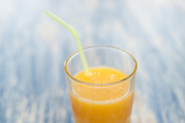 Orange juice in a glass with a straw on a blue wooden background of aqua color, top view and side view close-up
