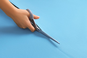 The hand of a young girl seamstress holds scissors and cuts smooth blue fabric. Sewing, tailoring concept with copy space