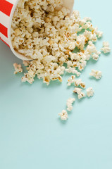 Vertical image.Fresh popcorn spilled from the paper bowl on the blue surface.Empty space for text