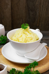 Mashed potatoes in white bowl or glass with parsley on wooden table.