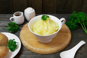 Mashed potatoes in white bowl or glass with parsley on wooden table.