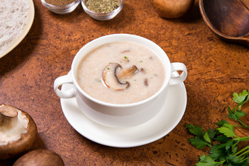 Cream mushroom soup in a white bowl on a brown background with ingredients. Selected focus.