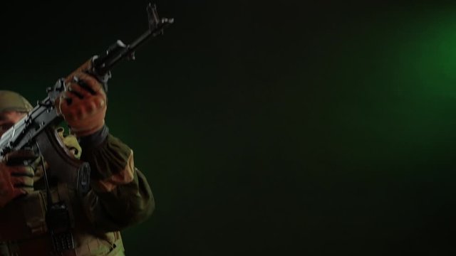 a rebel commando soldier in military clothing with a Kalashnikov rifle on a dark background takes aim