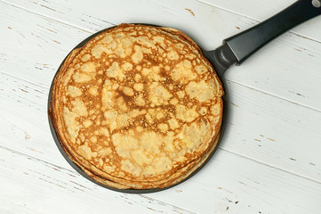 Stack of homemade pancakes on a frying pan on white wooden table. Top view. Russian pancake week concept.