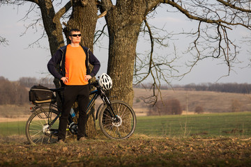 Obraz premium cyclist in an orange T-shirt stands on the sidelines and watches the sunset