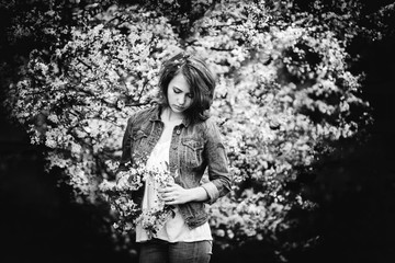 Dreamy cute girl of European appearance on a background of flowering trees. Flowering branches in the shape of a heart. Black and white photo.