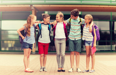 Obraz premium primary education, friendship, childhood and people concept - group of happy elementary school students with backpacks hugging outdoors