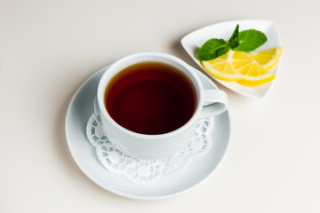 A white cup of black tea on a saucer and paper napkin, a small saucer with sliced lemon and mint