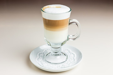 A glass of latte coffee on a white saucer with paper napkin