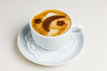 A white cup of cappuccino coffee on a white saucer and paper napkin. Coffee froth decorated with cinnamon moon and stars.