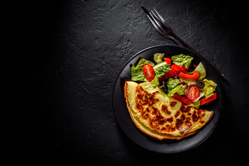 omelet with fresh mixed vegetables  salad on a black plate on Dark grey black slate background