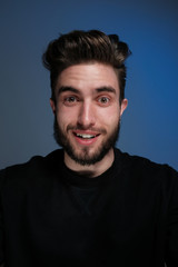 Fototapeta premium Beautiful caucasian young man portrait isolated on multicolored neon light backgroud. Young, smiling, surprised, screaming. Human emotions, facial expression concept. Trendy colors.Advertising concept