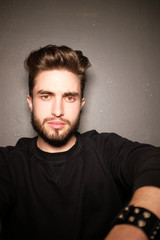 Obraz premium young handsome male with beard, mustache and trendy hairdo, wears casual grey sweater, has serious expression, poses in studio against gray background