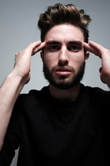 A young dark-haired man with a beard holds his head and shows different human emotions: hatred, fear, despair, horror, malaise, headache, clairvoyance. Close-up studio portrait of a man.