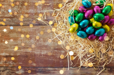 easter, confectionery and holidays concept - chocolate eggs in foil wrappers in straw nest on wooden background