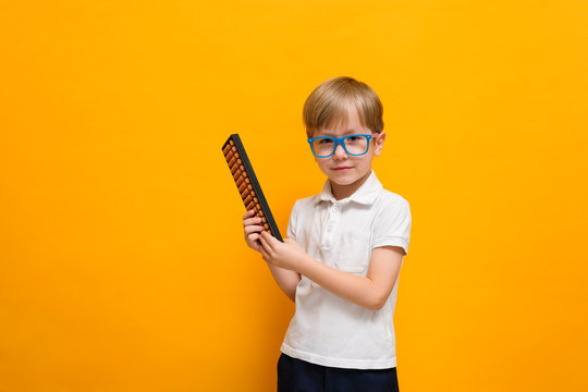 Cute little school boy in glasses holding abacus on yellow background. Mental arithmetic, math, mathematics