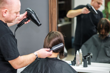 Close up of professional hairdresser is drying female hair, back view.