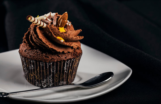 Closeup of chocolate cupcake with swirled buttercream icing and decoration on white saucer, isolated - Powered by Adobe