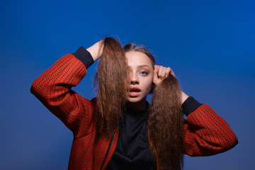 a young girl with blue eyes and blond long hair in a black T-shirt and red bomber jacket on a...