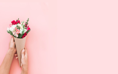 Roses bouquet in cone on pink background, flat lay, top view.