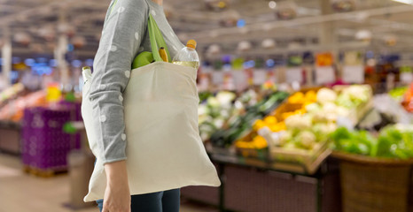 Fototapeta consumerism, eating and eco friendly concept - woman with white reusable canvas bag for food shopping over supermarket on background obraz