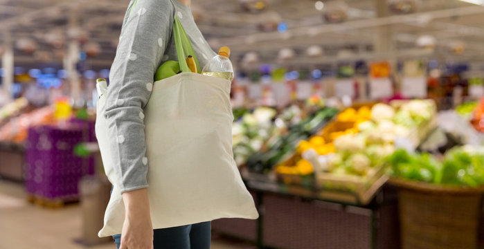 consumerism, eating and eco friendly concept - woman with white reusable canvas bag for food shopping over supermarket on background