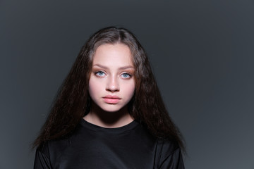 A close-up portrait of a young beautiful serious girl with blue eyes and brown hair in a black T-shirt and red bomber jacket 