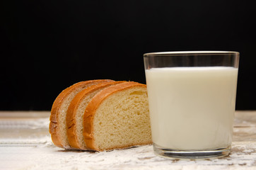 glass of milk and three slices of sliced loaf on a wooden background with flour on a black background with copy space