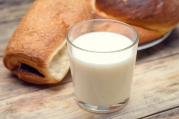 Glass of milk, rolls, sliced loaf on a wooden background