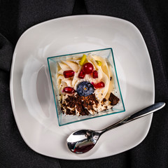 Individual portion of dessert in square glass on white saucer with teaspoon, top view